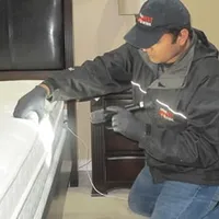 Bed bug inspection technician checking a mattress and bed frame for signs of infestation in Mobile, AL