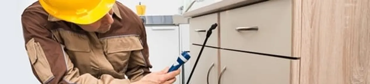 Roach exterminator applying treatment under kitchen cabinets in Mobile, AL