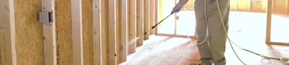Termite treatment technician applying spray along framing and unfinished walls in Mobile, AL